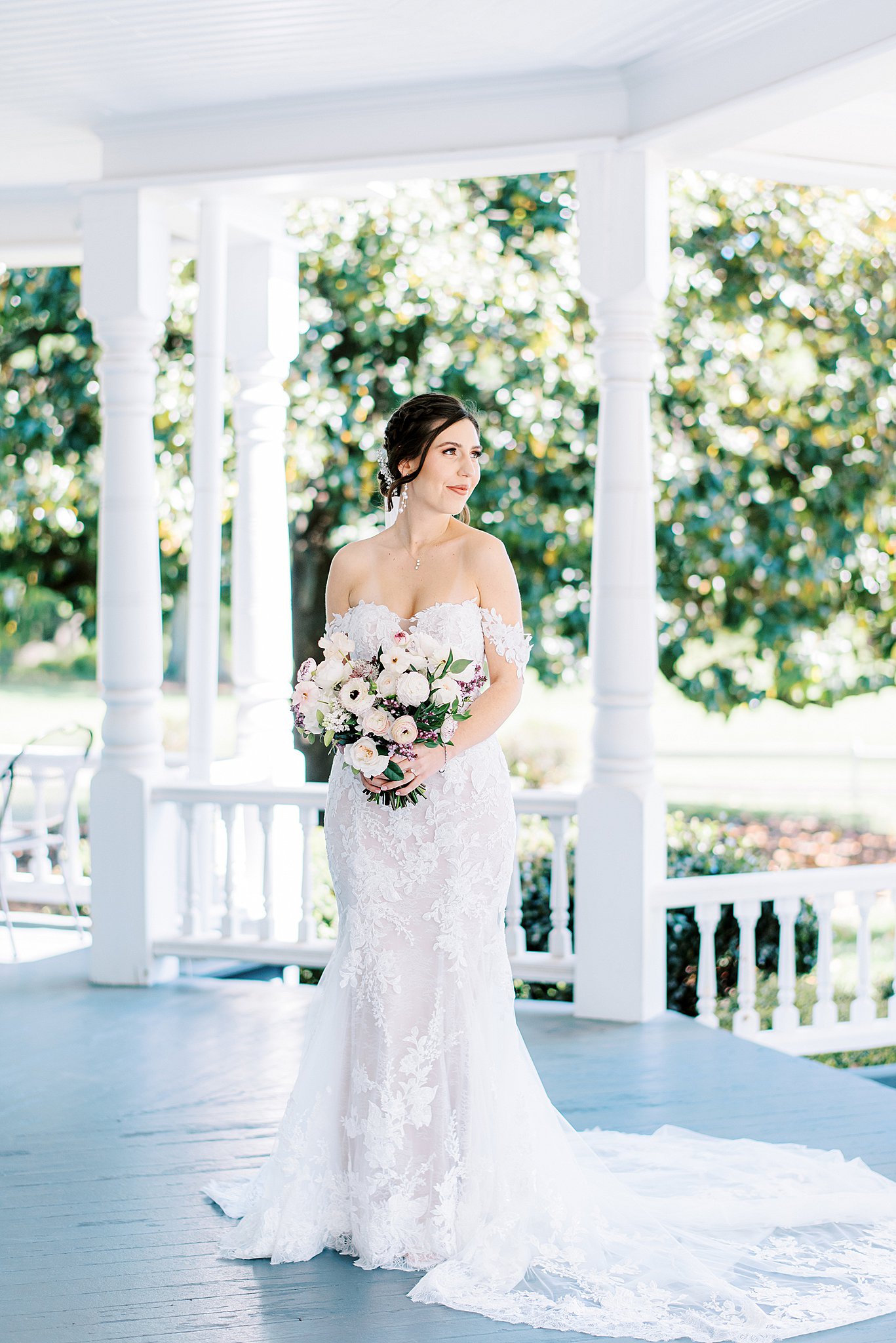 A bride stands under a gazebo in a white lace dress holding a bouquet Brawley Estate