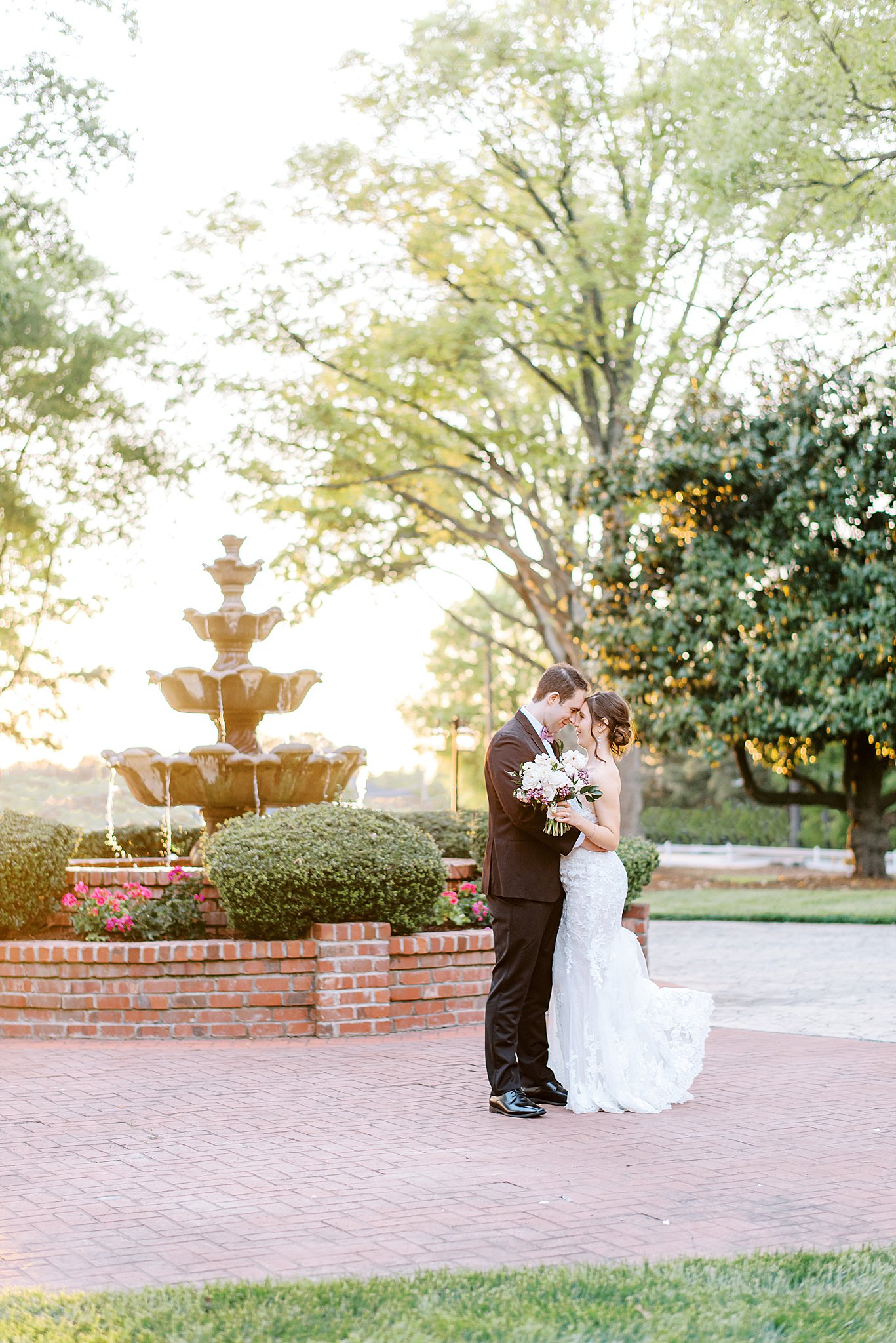 Newlyweds touch foreheads while hugging by a garden fountain at sunset Brawley Estate