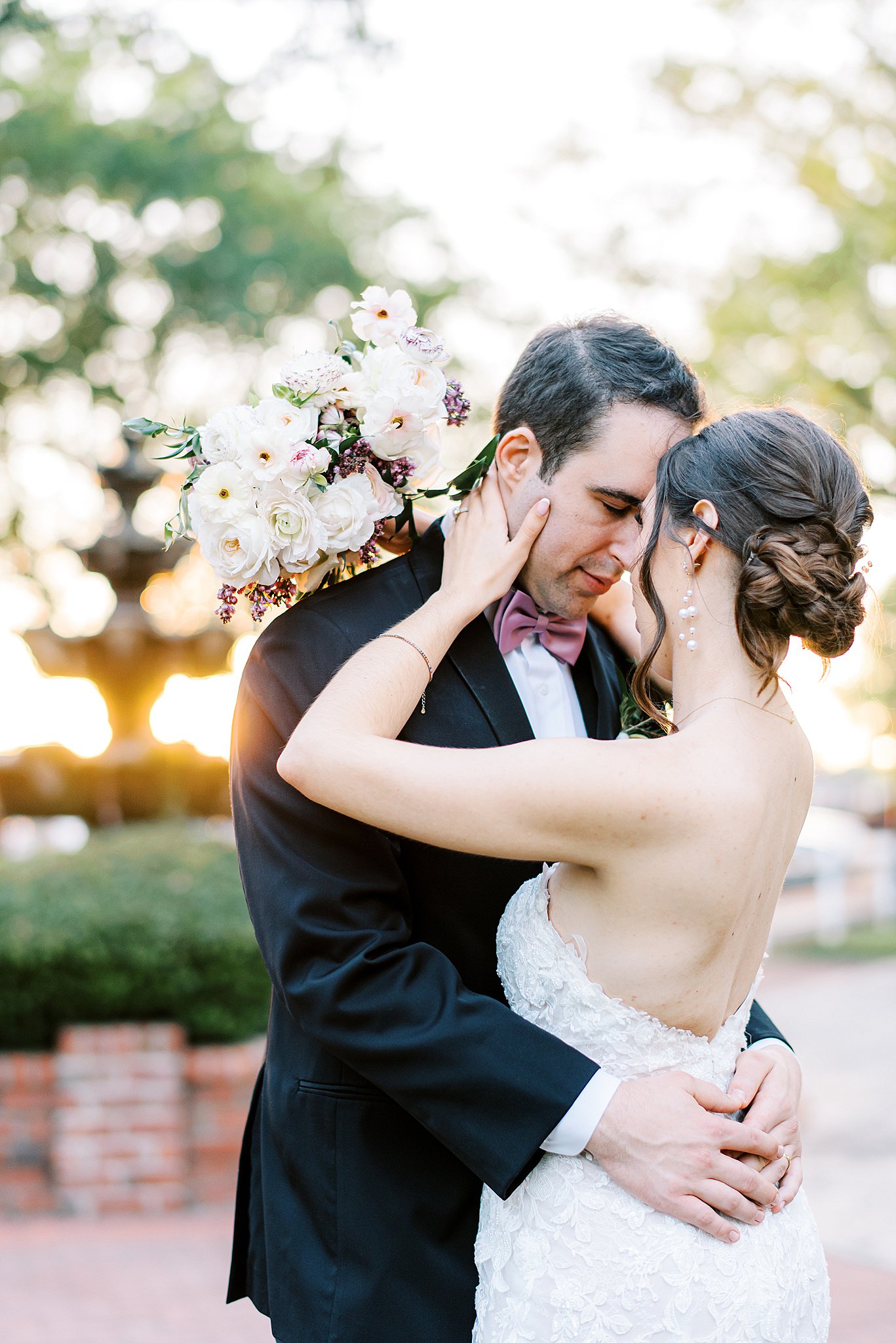Newlyweds embrace with a pink bowtie and lace dress at sunset in a garden at Brawley Estate