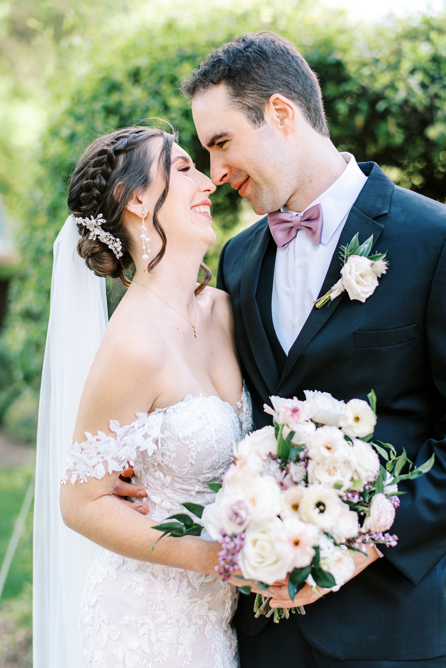 Newlyweds touch noses before a kiss while standing in a garden