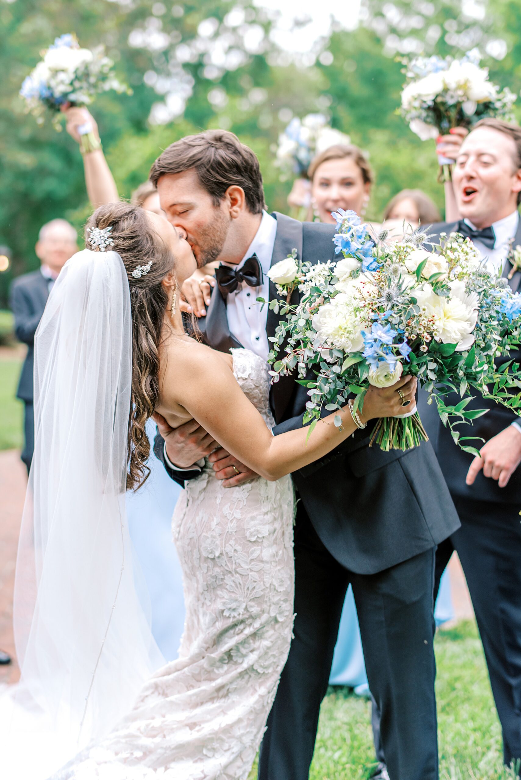 Newlyweds kiss for the first time while their wedding party cheer behind them holding white and blue florals at a charlotte country club wedding