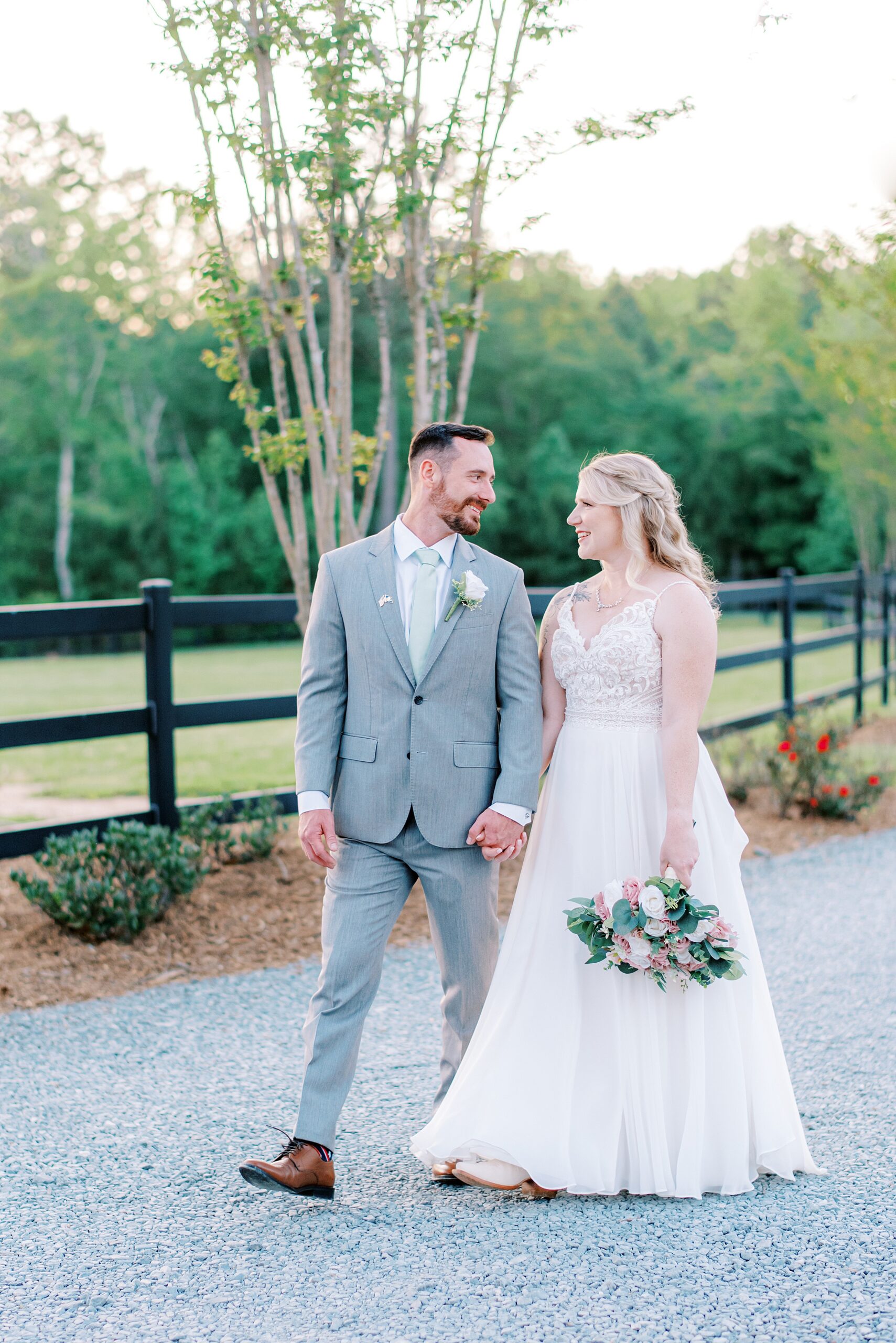 Newlyweds walk holding hands down a gravel path on a farm