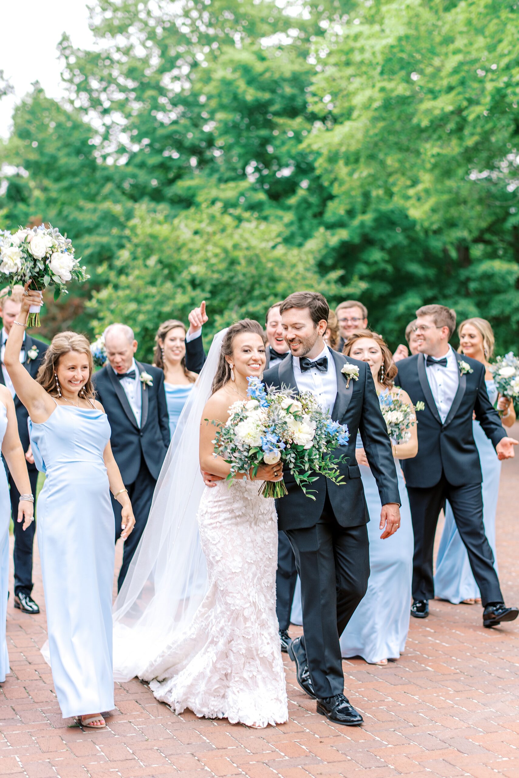 Newlyweds lead their wedding party while walking down a brick path